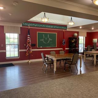 A spacious classroom with red walls, featuring tables, chairs, a chalkboard, and an American flag.