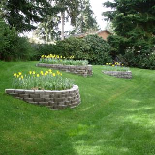 A landscaped garden featuring multiple retaining walls with flower beds on a grassy lawn.