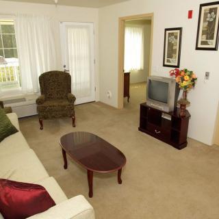 A cozy living room with a sofa, armchair, coffee table, and an old-style television.