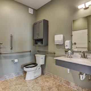 A modern accessible bathroom featuring a toilet, sink, and safety handrails.