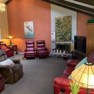 A cozy living room featuring multiple reclining chairs, a TV, and warm lighting.