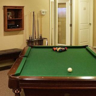 A billiards room featuring a green pool table with cue sticks in the background.