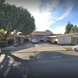 A quiet suburban residential street with houses, trees, and parked cars.
