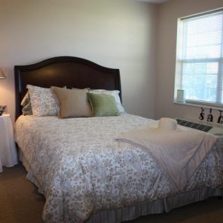 A cozy bedroom with a neatly made bed, soft pillows, and natural light from the window.