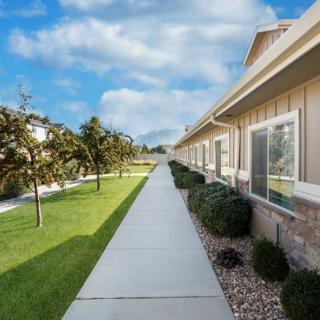 A clean sidewalk bordered by trees and grass, running alongside residential housing on a clear day.
