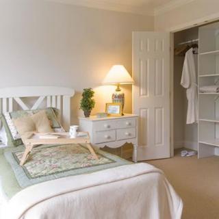 A cozy bedroom with a neatly made bed, a nightstand with a lamp, and an open closet.
