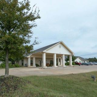 A single-story building with columns, surrounded by a grassy area and parking lot.