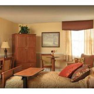 A cozy bedroom with warm tones, featuring a bed, a wooden wardrobe, and a small table by the window.