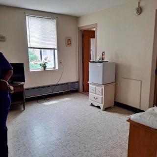 A simple room with a window, small fridge, and basic furnishings.