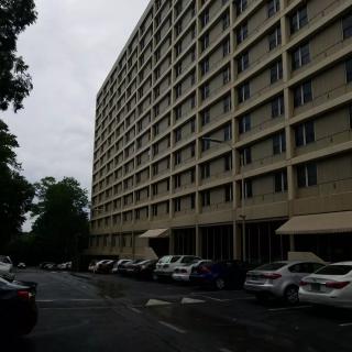 A view of a tall apartment building with parked cars in the foreground on an overcast day.