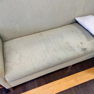A stained couch with a single white pillow in an indoor setting.