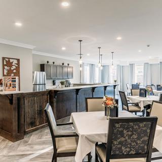 A modern dining area with neatly arranged tables and chairs, adjacent to a kitchen space with stylish lighting.