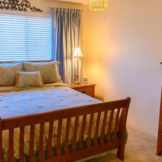 A cozy bedroom with a wooden bed frame, bedside lamp, and sunlight filtering through curtains.