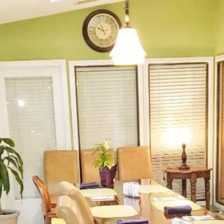 A cozy dining room with a green accent wall, featuring a table surrounded by chairs, a side lamp, an indoor plant, and a clock mounted above.