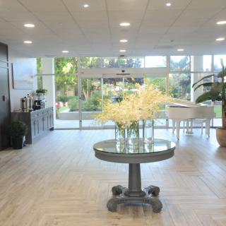 A modern lobby with a central table decorated with flowers, illuminated by natural light.