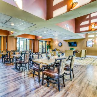 A spacious dining area with ample natural light, featuring several tables and chairs on a wooden floor.
