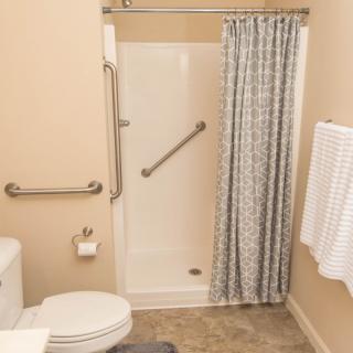 An accessible bathroom with a shower, grab bars, toilet, and towels.