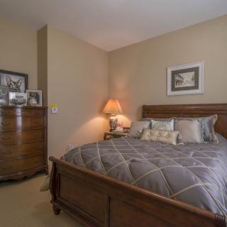 A cozy bedroom with a wooden bed and dresser, softly illuminated by a bedside lamp.