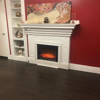 A cozy living room featuring a decorative fireplace set against a bold red wall, with shelves displaying various ornaments.