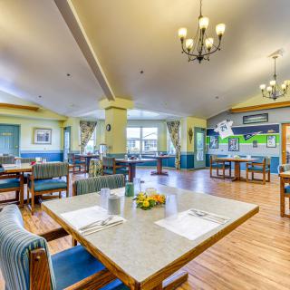 A well-lit and spacious dining area in a senior living facility, featuring neatly arranged tables and comfortable seating.