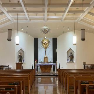 Interior view of a church facing the altar with wooden pews and statues on either side.