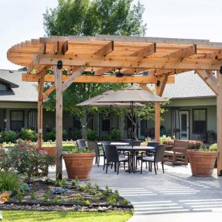 A patio area featuring a wooden pergola, outdoor seating, and lush landscaping.