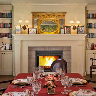 An elegant dining room with a cozy fireplace, surrounded by bookshelves and set for a formal dinner.