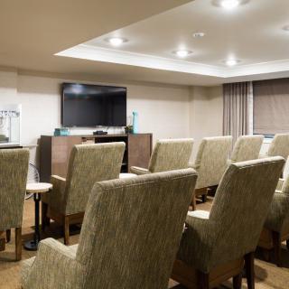 A well-lit conference room featuring rows of upholstered chairs facing a large television screen.