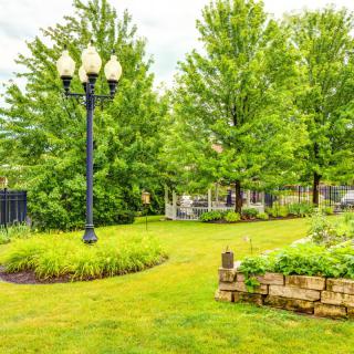 A beautifully landscaped park with lush green grass, mature trees, and a classic lamp post.