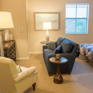 A cozy living room with a sofa and armchair, adorned with a lamp and window view.