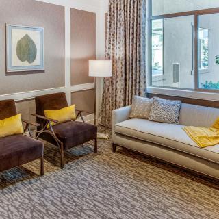 A cozy living room with a sofa and two chairs, decorated in neutral tones with pops of yellow accents.