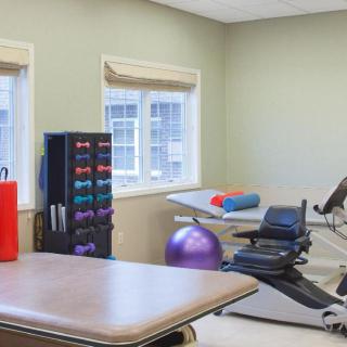 A rehabilitation therapy room equipped with exercise equipment, including dumbbells, an exercise ball, and a treatment table.