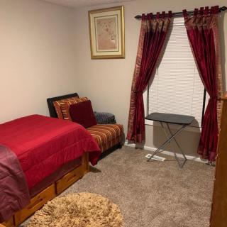 A cozy bedroom with red bedding, a chair, and decorative curtains.