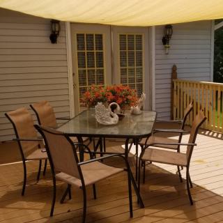 A cozy outdoor patio with a glass table and chairs under a sunshade.