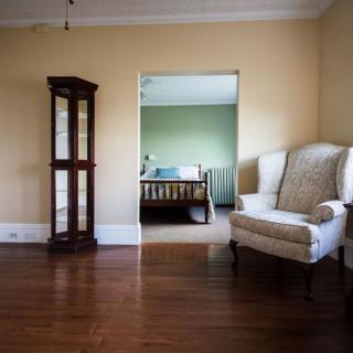 A cozy living room with a view into a bedroom, featuring hardwood floors, an elegant armchair, and a display cabinet.