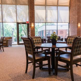 A spacious lobby area with a table and chairs, illuminated by natural light streaming through large windows.