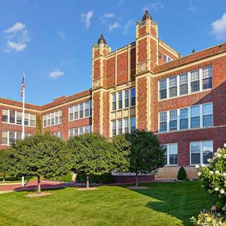 A historic brick school building with well-maintained landscaping under a clear blue sky.