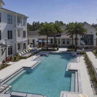 A modern apartment complex featuring a swimming pool surrounded by palm trees.