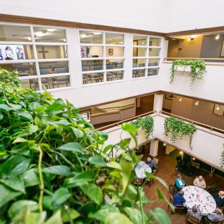 An indoor atrium with plants, balconies, and a dining area filled with people.