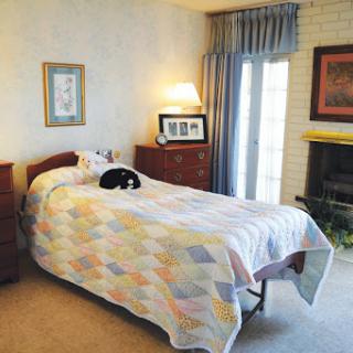 A cozy bedroom featuring a single bed with a colorful quilt, a sleeping cat on the bed, and warm lighting.