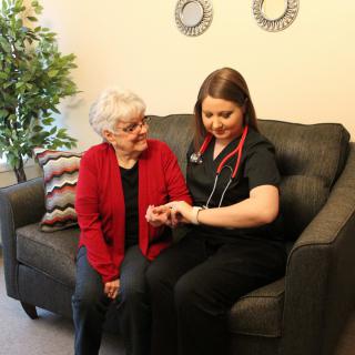 A caregiver or nurse is assisting an elderly woman in a living room setting, providing healthcare services.