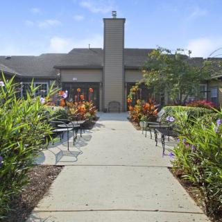 A landscaped garden with a pathway leading to a building, surrounded by chairs and vibrant flowers.