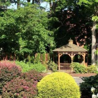 A peaceful garden scene featuring a wooden gazebo surrounded by lush greenery.