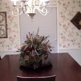 A dining room with floral wallpaper, featuring a wooden table with a centerpiece and an elegant chandelier overhead.
