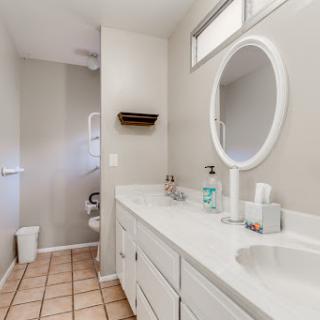 A clean and modern bathroom featuring a double vanity with a round mirror, tile flooring, and ample natural light.