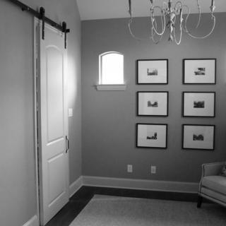 A cozy bedroom featuring a barn-style sliding door, a small window, a chandelier, and neatly arranged framed pictures on the wall.