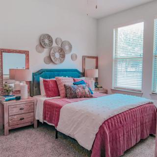 A cozy bedroom with stylish decor, featuring a bed, nightstands, lamps, and decorative wall art.