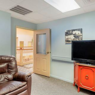 A cozy living room with a leather sofa, television, and an open door leading to another hallway.