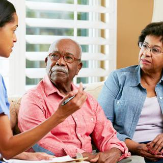 A nurse engages in a discussion with an elderly couple in a home setting.