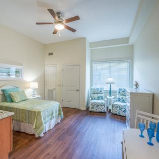 A modern bedroom with a bed, two armchairs, and a ceiling fan.
